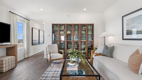 Spacious living room decorated in natural wood tones, white couches and a large bookshelf full of green books