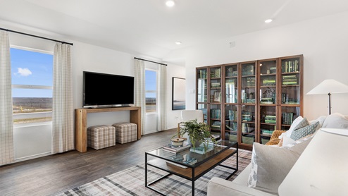 Spacious living room decorated in natural wood tones, white couches and a large bookshelf full of green books