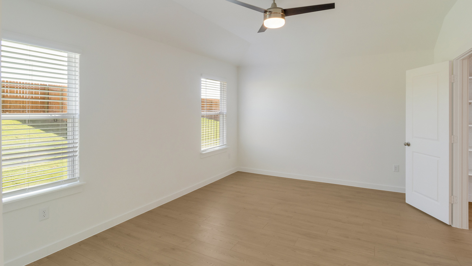 Spacious main bedroom with laminated wood flooring and two windows.
