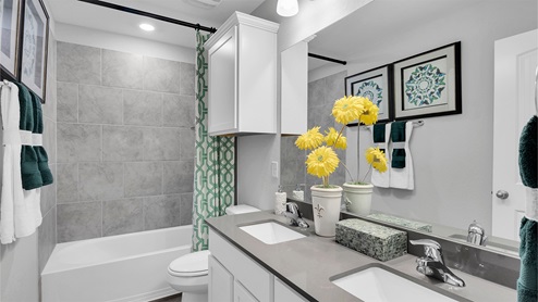 Creekfall model home secondary bathroom with double vanity sink and tub-shower combo.