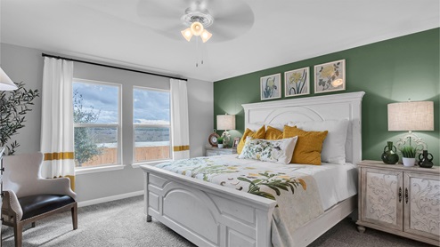 Creekfall model home primary bedroom with king size bed and carpet flooring.