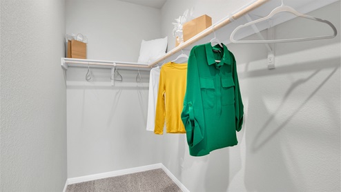 Creekfall model home primary bedroom walk-in closet with carpet flooring and spacious room.