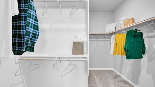 Creekfall model home primary bedroom walk-in closet with carpet flooring and spacious room.