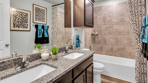 Three Creeks Colt Creek model home secondary bathroom with double vanity and mirror and a bathtub and shower combo.
