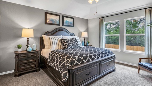 Three Creeks Colt Creek model home primary bedroom with a king bed and carpet flooring.