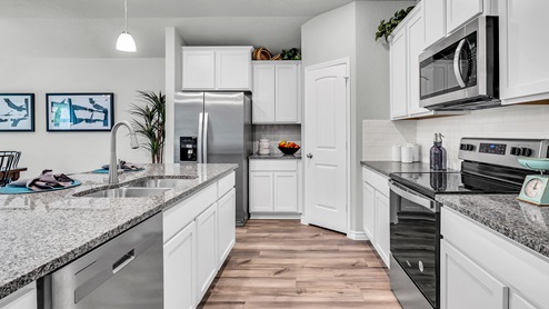 Three Creeks Colt Creek model home kitchen with white cabinets and granite countertops.