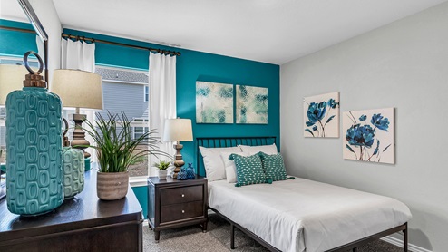 Three Creeks Colt Creek model home secondary bedroom with a full-size bed and accent decor.