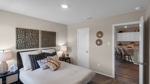 Park Meadows model home secondary bedroom with a full-size bed and view into the kitchen.