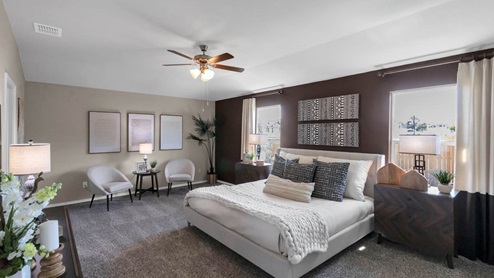 Park Meadows model home primary bedroom with a king bed and two lounge chairs.