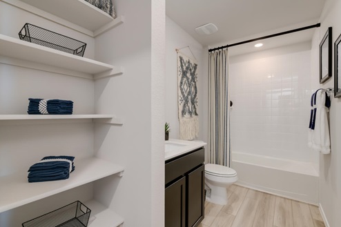 Willow Glenn model home secondary bathroom with storage shelving and bathtub and shower combo.