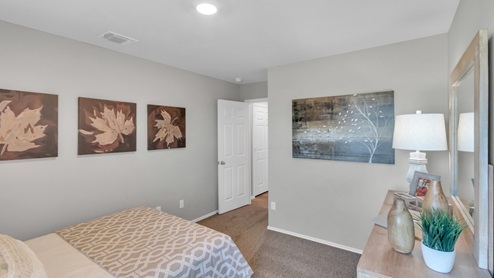 Pecan Creek model home secondary bedroom with a full-size bed and dresser.