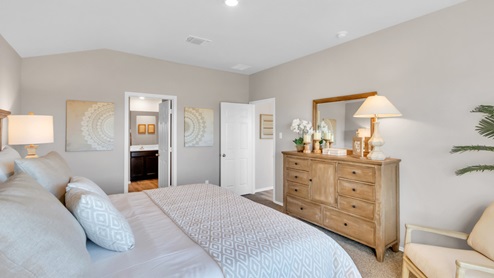 Pecan Creek model home primary bedroom with a king bed and view into primary bathroom.