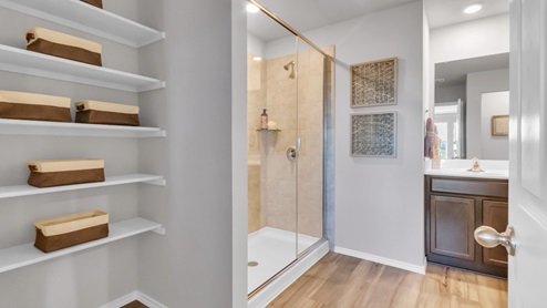 Pecan Creek model home primary bathroom with storage shelving and walk-in shower.