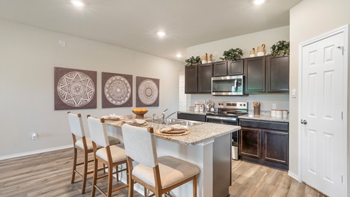 Pecan Creek Model Texas Cali kitchen with view of center kitchen island and front entrance hallway.