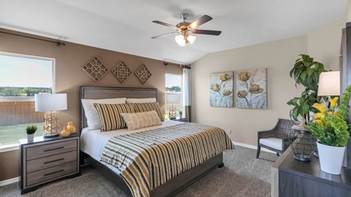Warrior's Legacy model home primary bedroom with a king bed and carpet flooring.