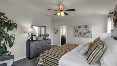 Warrior's Legacy model home primary bedroom with a king bed and view of the primary bathroom.