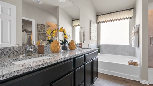 Warrior's Legacy model home primary bathroom with double vanity sinks and mirror and a soaking bathtub.