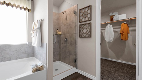 Warrior's Legacy model home primary bathroom with a soaking bathtub and walk-in shower.