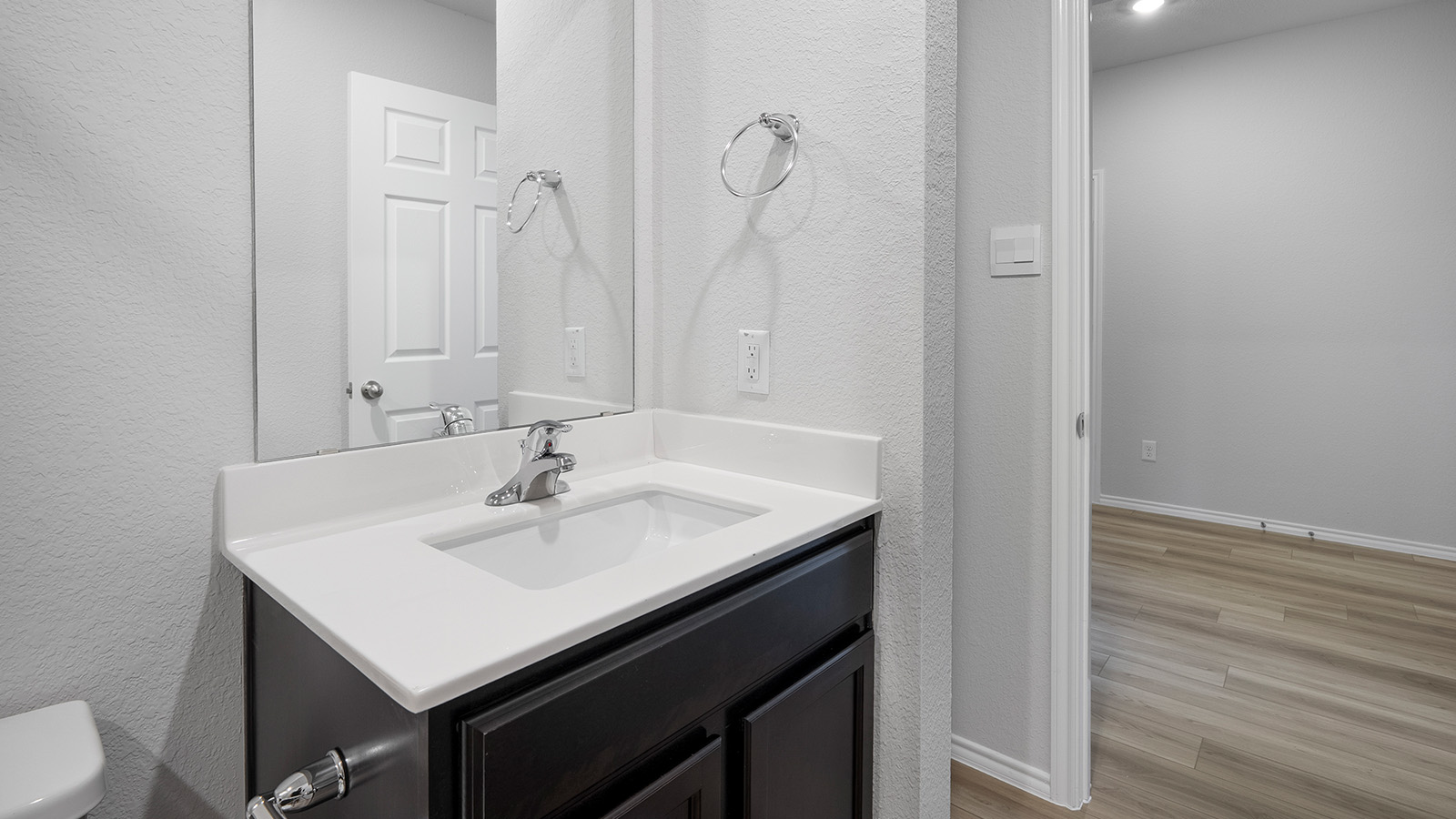 Creekside Hills model home secondary bathroom with single vanity sink and mirror with view of hallway.