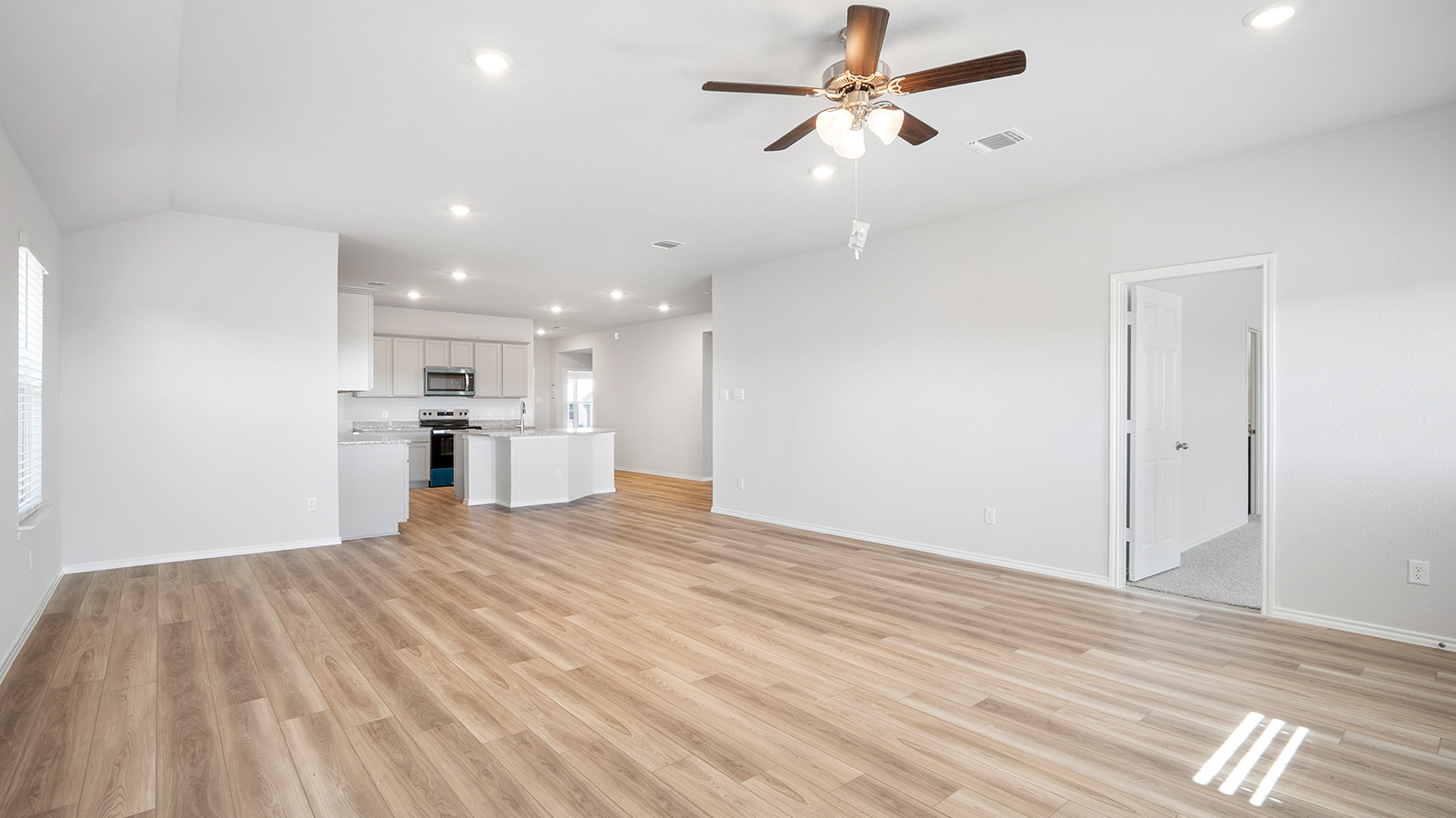 Creekside Hills model home living room with vinyl plank flooring and view of kitchen and primary bedroom.