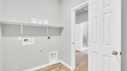 Village at Nolan Heights model home utility room with storage shelving and washer and dryer connections.