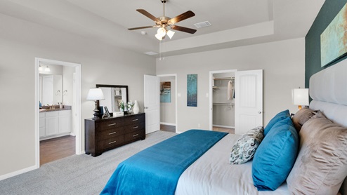 Sterling Meadows model home primary bedroom with a king bed and view of a walk-in closet and primary bathroom.