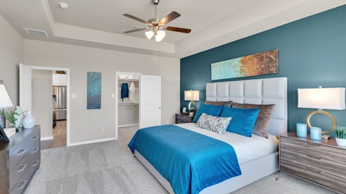 Sterling Meadows model home primary bedroom with a king bed and view of a walk-in closet.