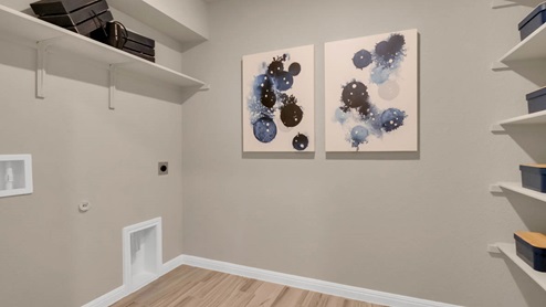 Delaware Springs model home utility room with storage shelving and washer and dryer connections.