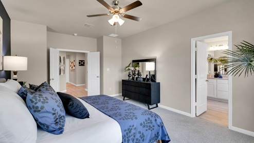 Delaware Springs model home primary bedroom with a king bed and view of the primary bathroom.