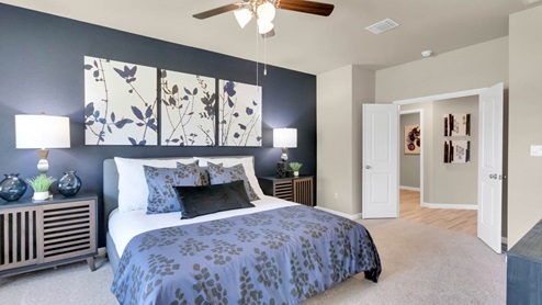 Delaware Springs model home primary bedroom with a king bed and carpet flooring.