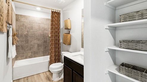 Mitchell Farm model home secondary bathroom with storage shelving and a bathtub and shower combo.