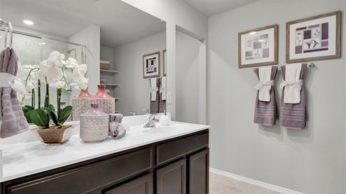 Reynolds Crossing model home primary bathroom with white cultured marble countertops and dark cabinets.