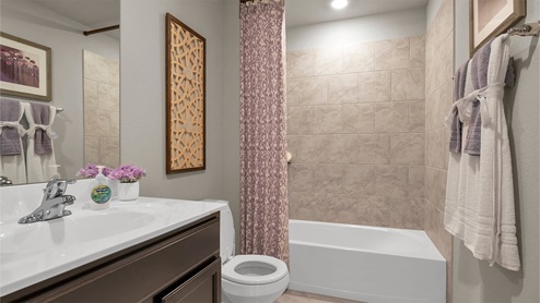 Reynold Crossing model home secondary bathroom with white cultured marble countertops and dark cabinets and ceramic tile flooring.