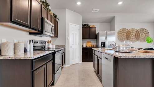 Victory Ranch model home kitchen with dark cabinets and granite countertops and tile flooring.