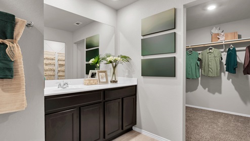 Victory Ranch primary bathroom with white cultured marble countertops and dark cabinets and tile flooring.