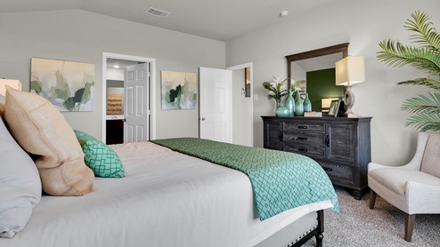 Victory Ranch primary bedroom with green accent wall and king-sized bed and carpet flooring.