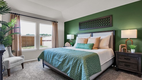 Victory Ranch primary bedroom with green accent wall and king-sized bed and carpet flooring.