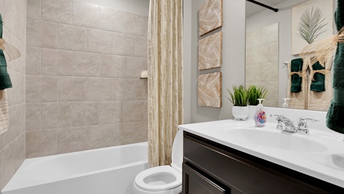 Victory Ranch secondary bathroom with tile surround on tub and shower combo, white cultured marble countertops and dark cabinets.