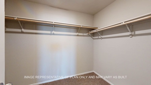 Fargo primary bedroom walk-in closet with carpet flooring and storage shelf and hanging rod.