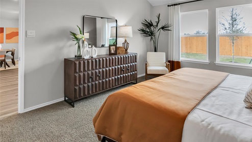 Eastern Wells Model Home primary bedroom with large dresser and windows offering natural light.