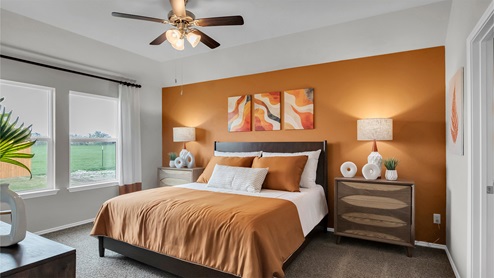 Eastern Wells Model Home primary bedroom with window and rust colored accent wall and king-sized bed.