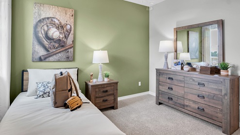 Country Meadows Model home secondary bedroom with carpet flooring and staged with furniture and decorations.