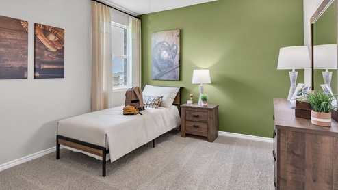 Country Meadows Model home secondary bedroom with carpet flooring and staged with furniture and decorations.