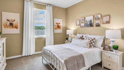 Country Meadows Model home secondary bedroom with carpet flooring and staged with furniture and decorations.