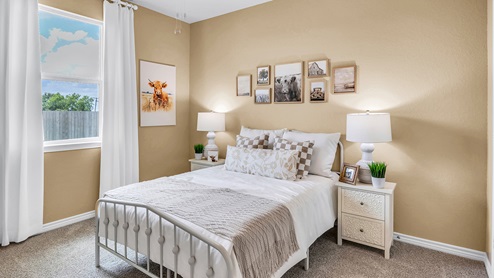 Country Meadows Model home secondary bedroom with carpet flooring and staged with furniture and decorations.