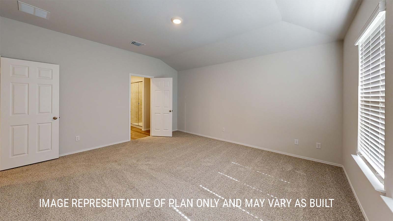 Grace primary bedroom with carpeted flooring and view of primary bathroom.