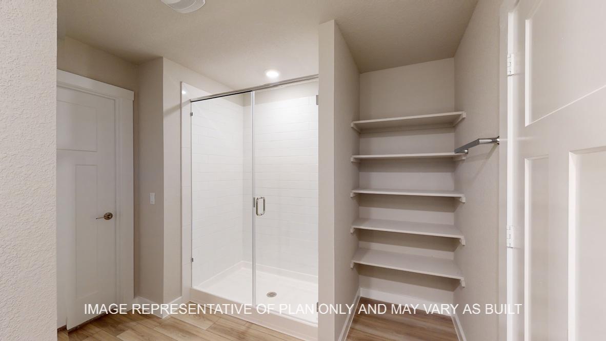 Easton primary bath with glass shower enclosure and storage shelves.