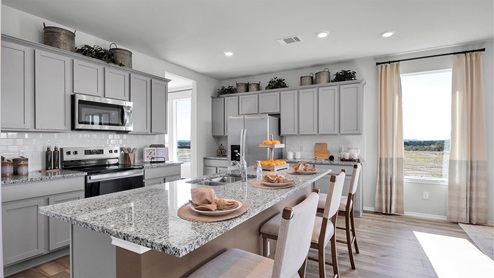 Turnbo Ranch Traditions model home kitchen with granite tops and gray cabinets.