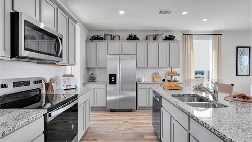 Turnbo Ranch Traditions model home kitchen with granite tops and gray cabinets.