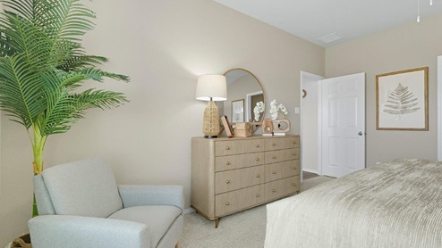 Mesa Ridge model home primary bedroom with carped flooring and light brown dresser.
